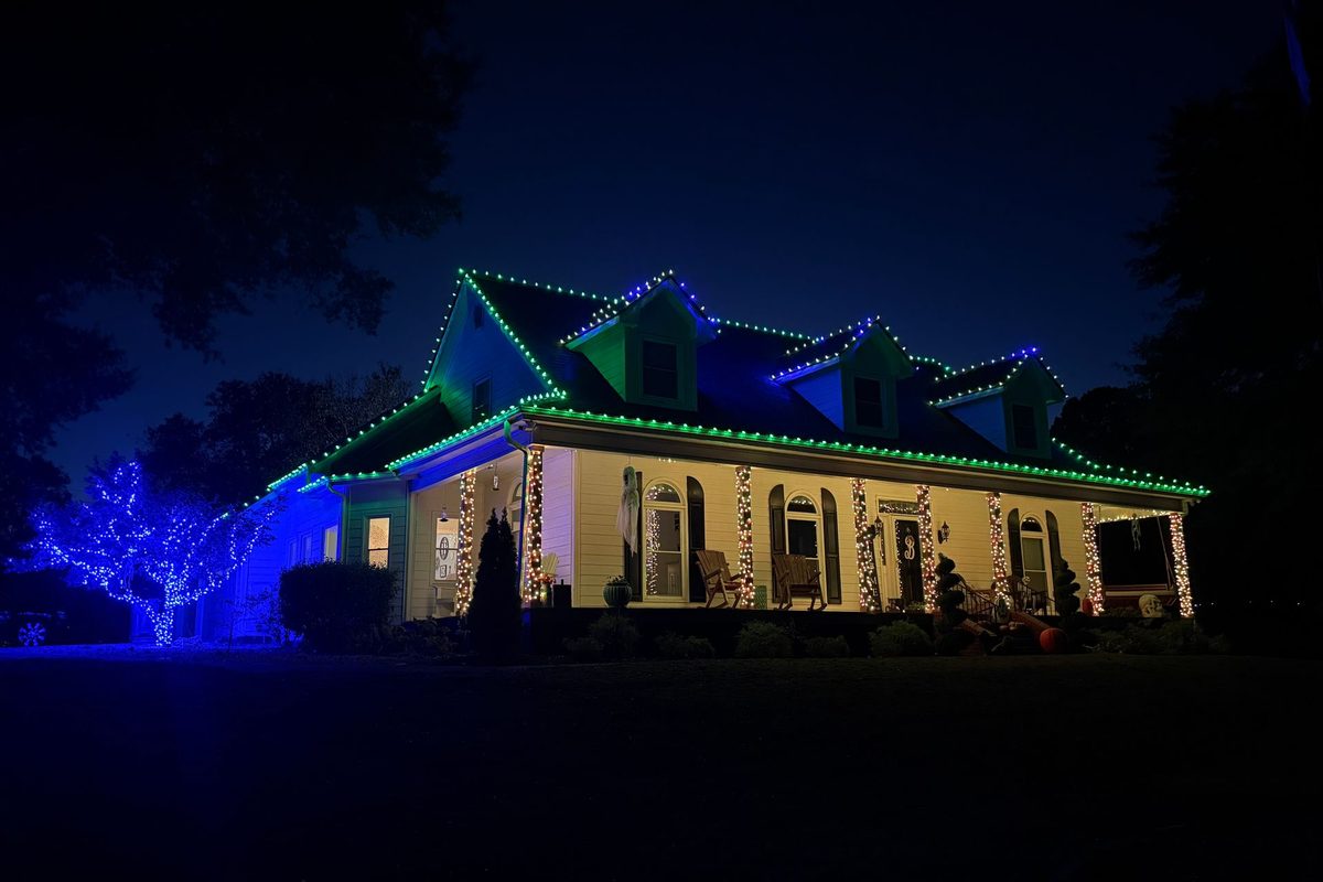 A house lit in blue and green from a permanent LED roofline system at night